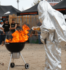 Feuerwehrmann im Vollschutzanzug demonstriert Flammenbildung im Grill bei Verwendung von Spiritus